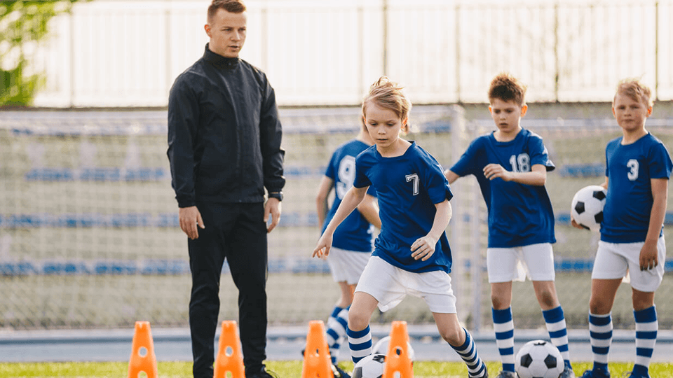 Young boys training with footballs and cones with coach guidance.